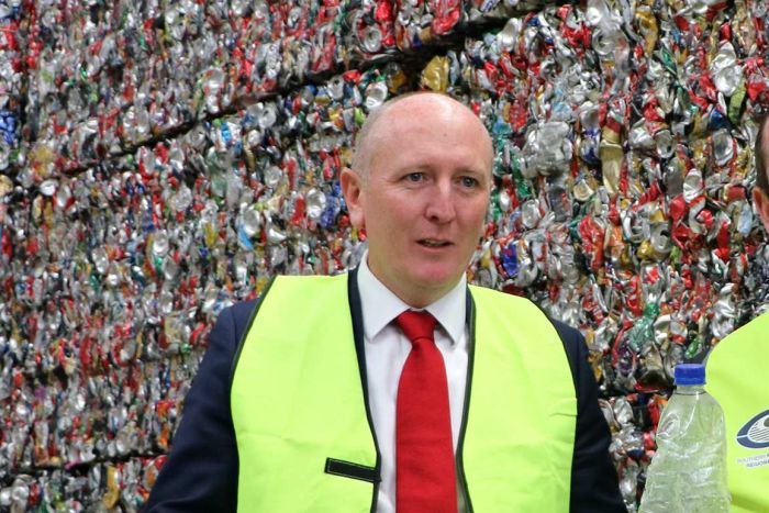Mark McGowan and Mr Dawson hold up empty bottles in front of a giant pile of crushed cans.