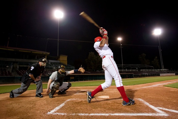 A baseball player swings at a pitch while the catcher and umpire look on.