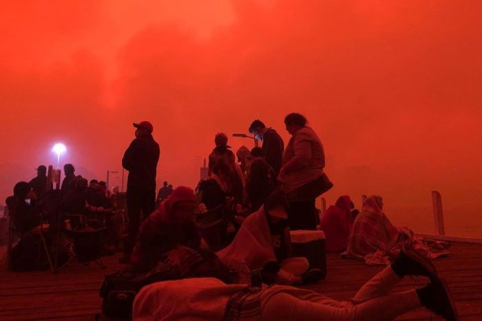 People seek refuge at Mallacoota Wharf as bushfires close in People seek refuge at Mallacoota Wharf under an orange sky.