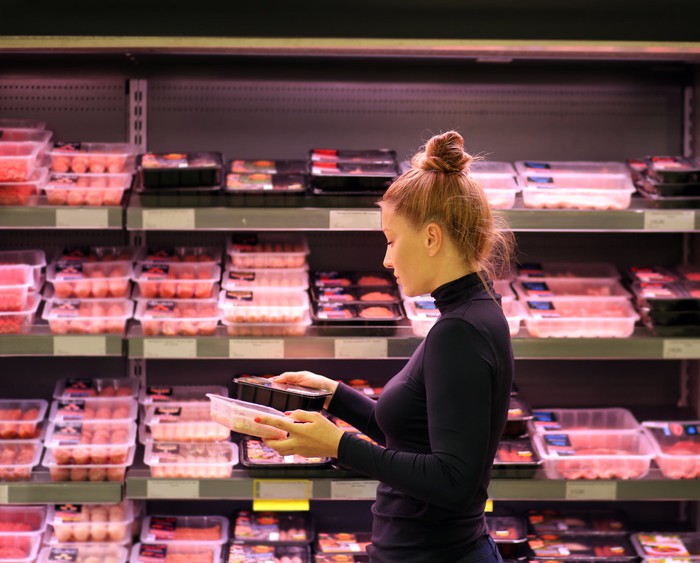 A woman examines packaged meat in a grocery store.