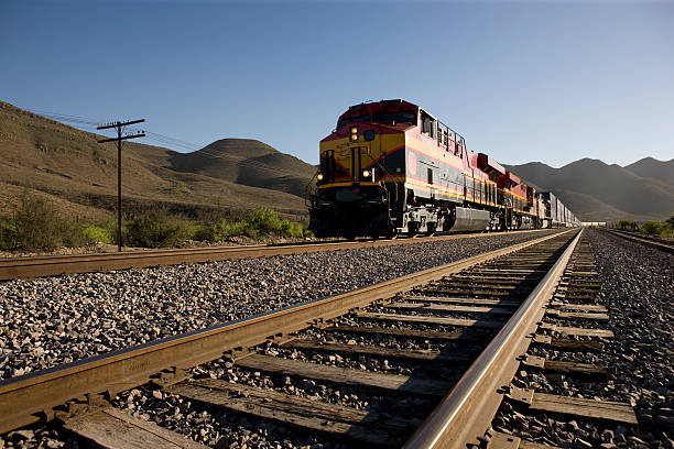 angled view of train tracks with oncoming freight train - cargo train stock pictures, royalty-free photos & images